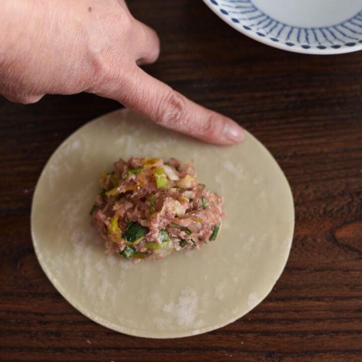 Wetting the edge of filled dumpling wrapper with water using a finger.