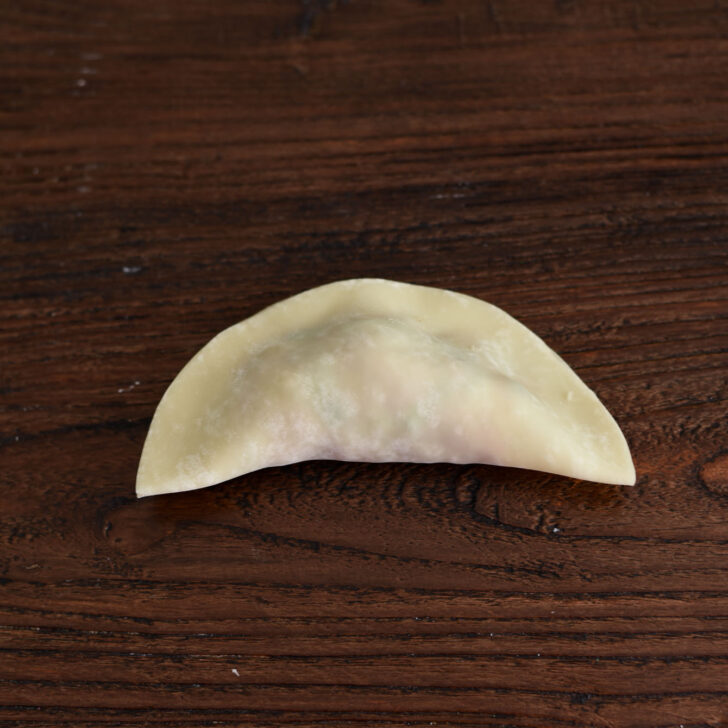 Folding dumpling wrapper in half with filling inside.