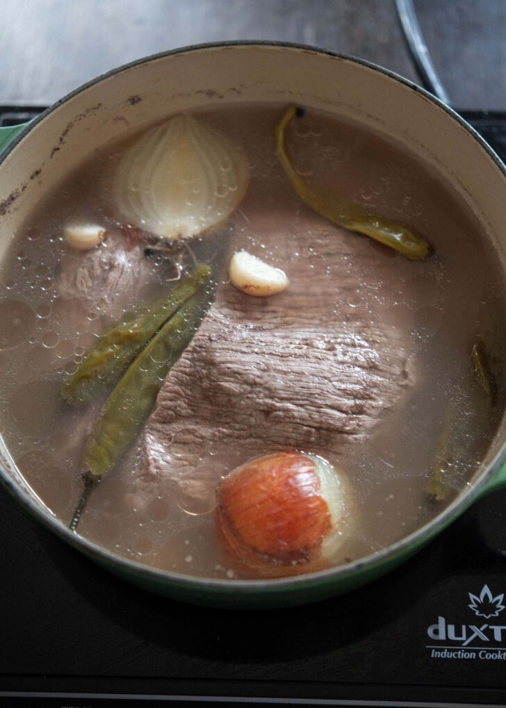 A chunk of beef brisket simmering with aromatics in a pot.