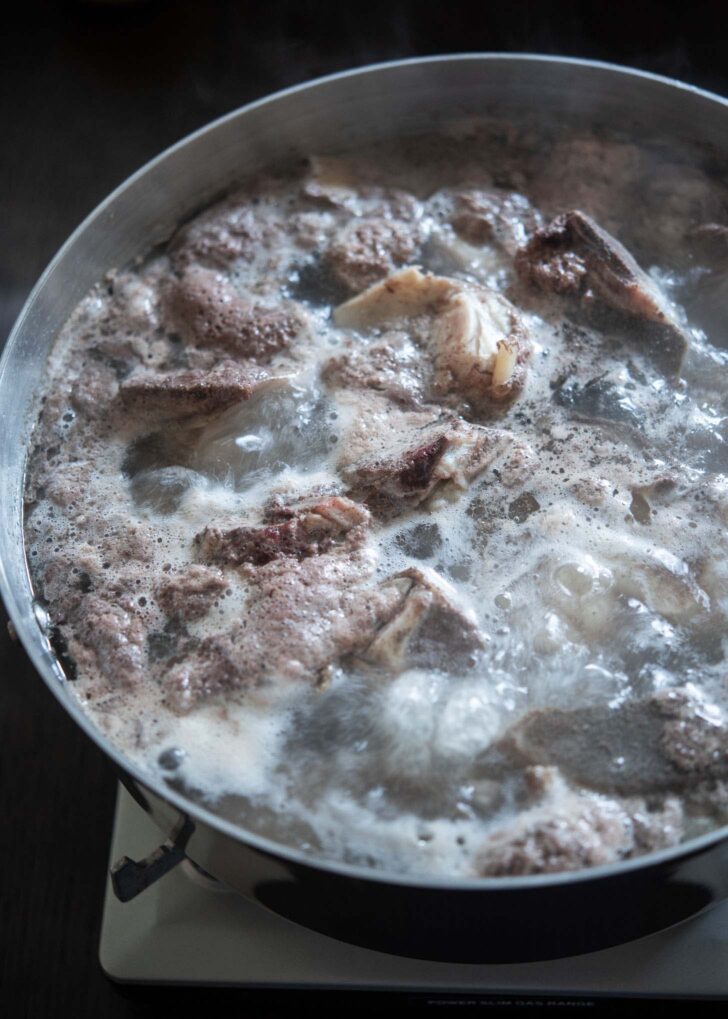 Initial boiling of beef bones to remove scum and impurities.