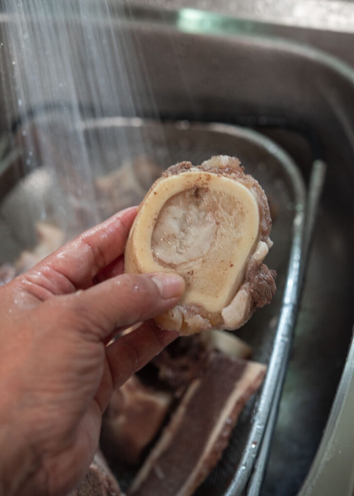 Parboiled ox bones with marrow being rinsed under water.