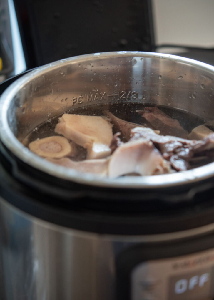 Parboiled bones covered with cold water inside of an instant pot.