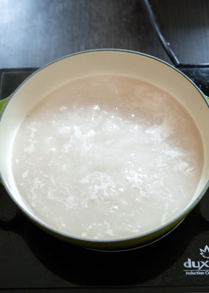 Milky white bone broth heated in a pot.