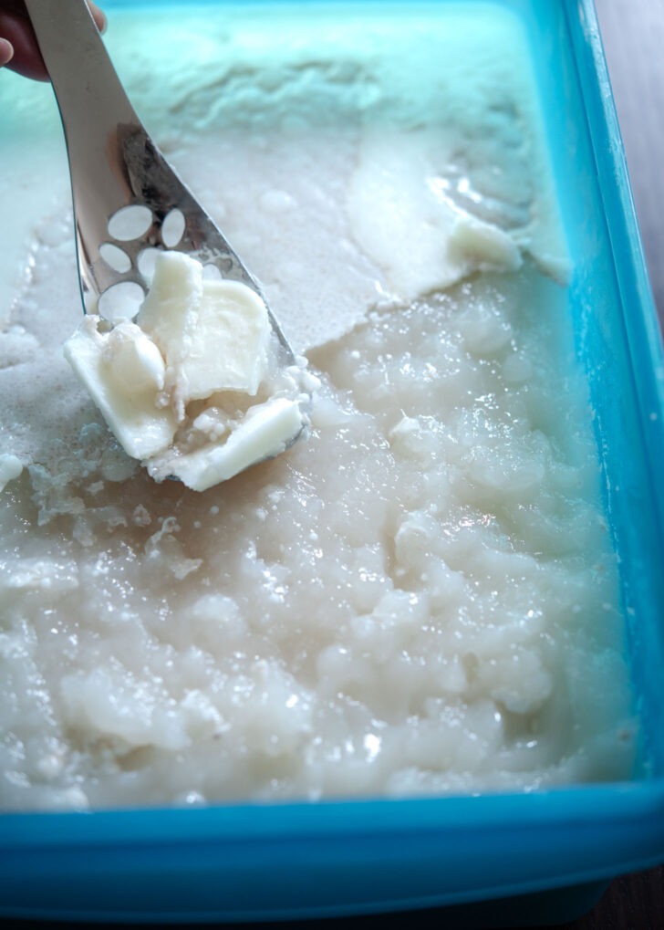 A slotted spoon scooping off the fat from the broth gelatin.