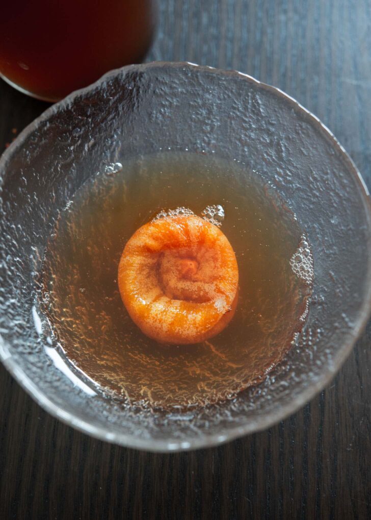 Flattened dried persimmon soaking in Korean cinnamon punch in a bowl.