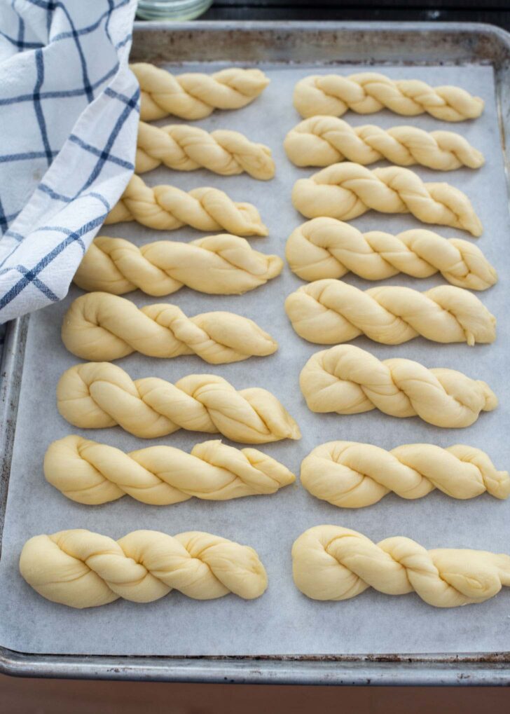 Twisted donut doughs are laid together on a pan lined with parchment paper.