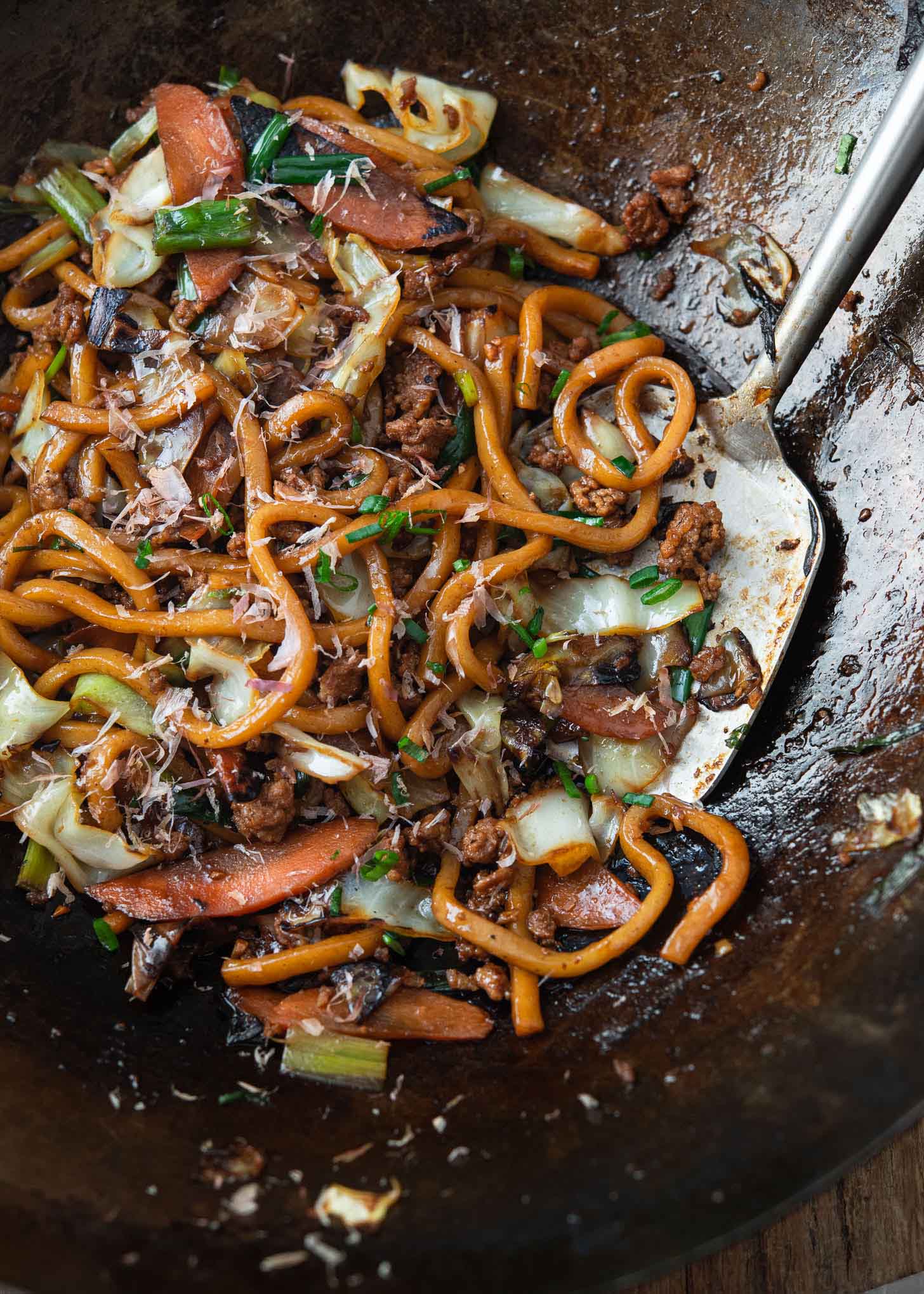 Yaki udon noodles stir-fried with pork and vegetables in a wok.