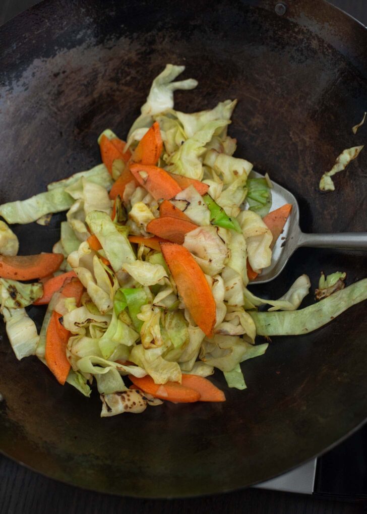 Cabbage onion, and carrot slices stir frying in a wok to make Yaki Udon.