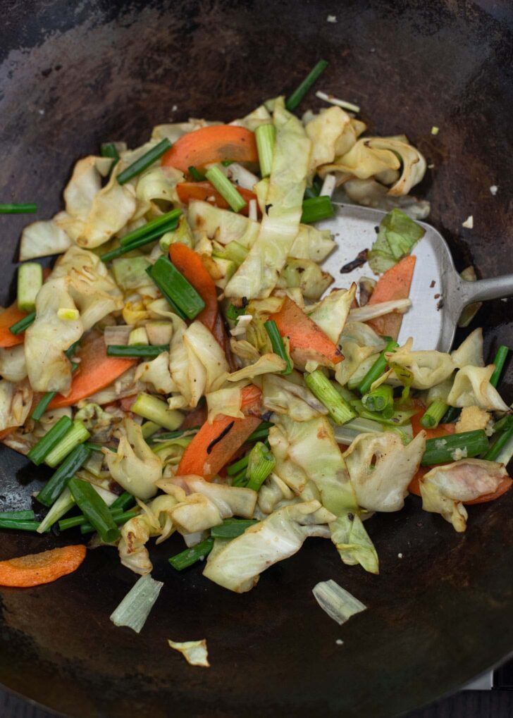 Green onion added to stir-fried vegetables in a wok.