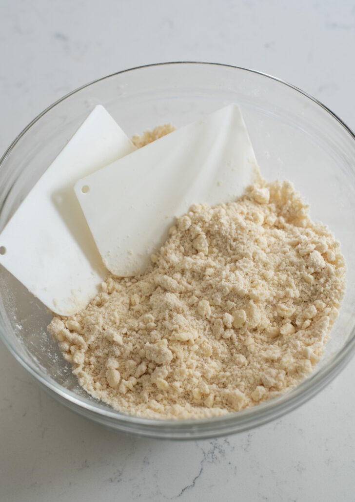 Pie dough mixture blended to coarse crumb using pastry scrapers.