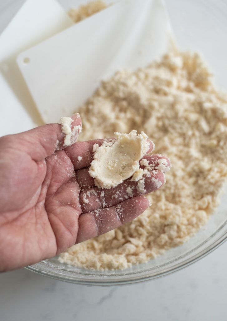 Pressing dry pie dough mixture with fingers.