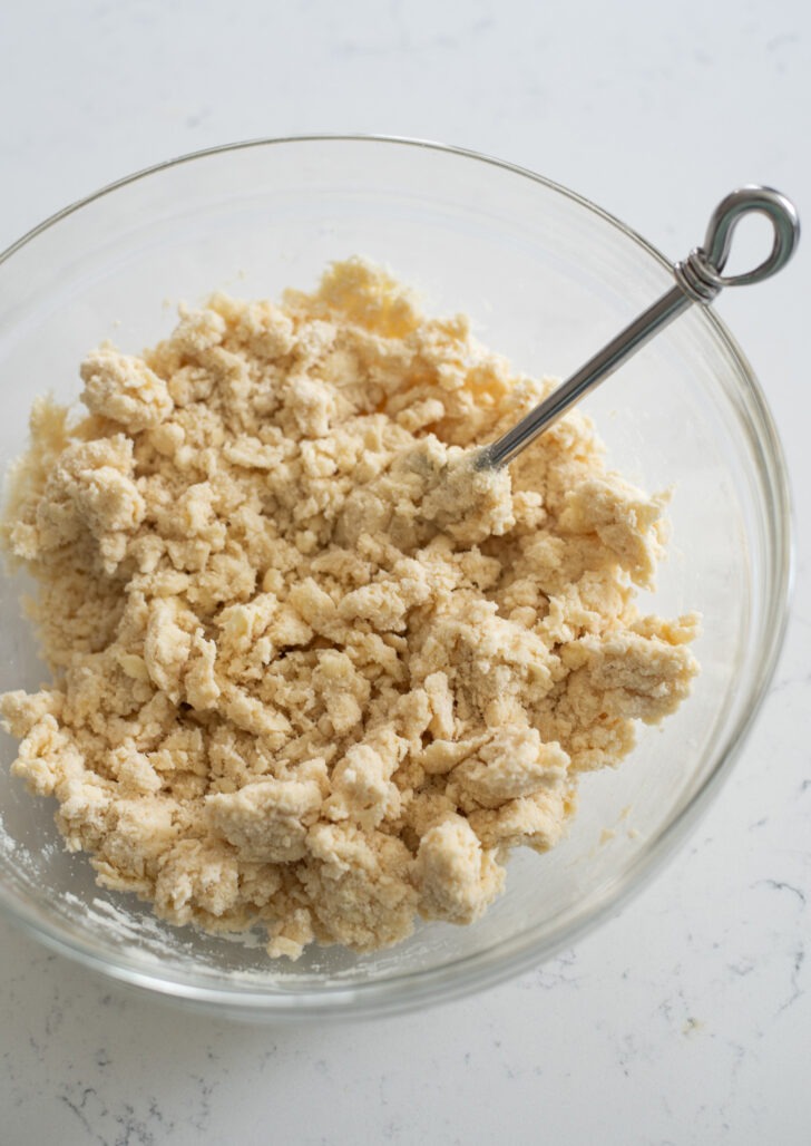 Pie dough mixture moistened in a mixing bowl.