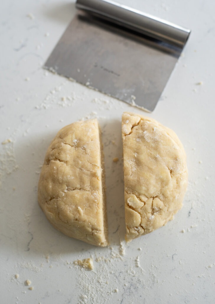 Pie dough disk cut into half with a baking scraper.