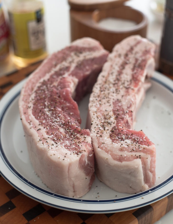 Two chunks of pork belly seasoned with salt and pepper.