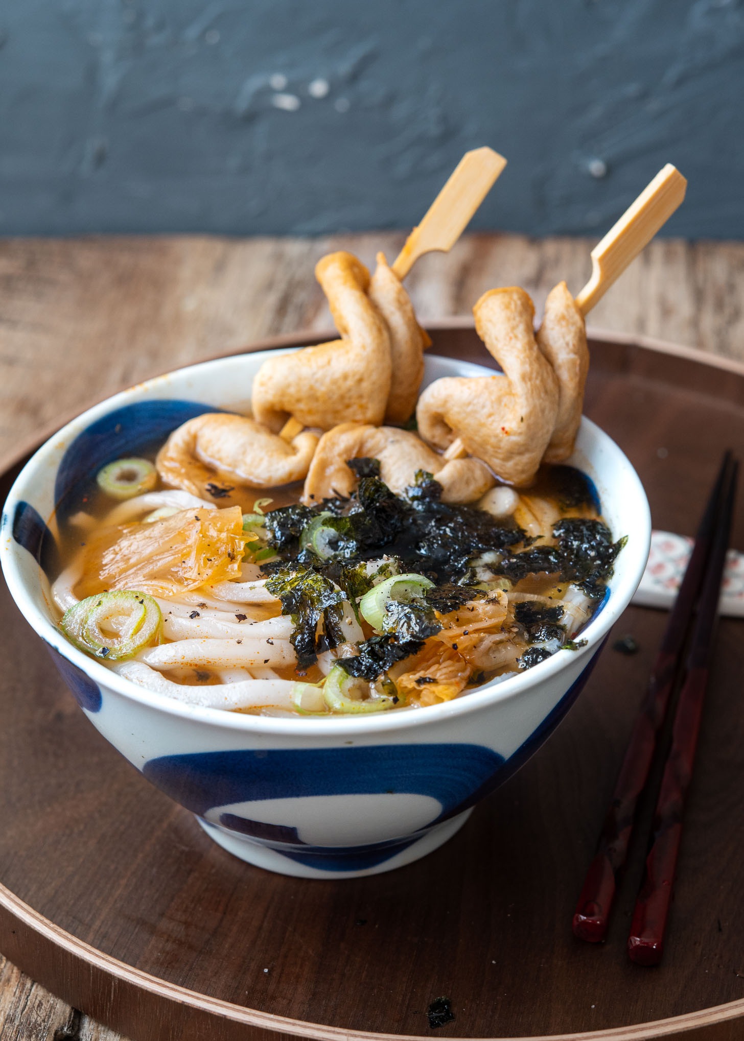 Kimchi udon noodle soup with fish cake skewers in a bowl.