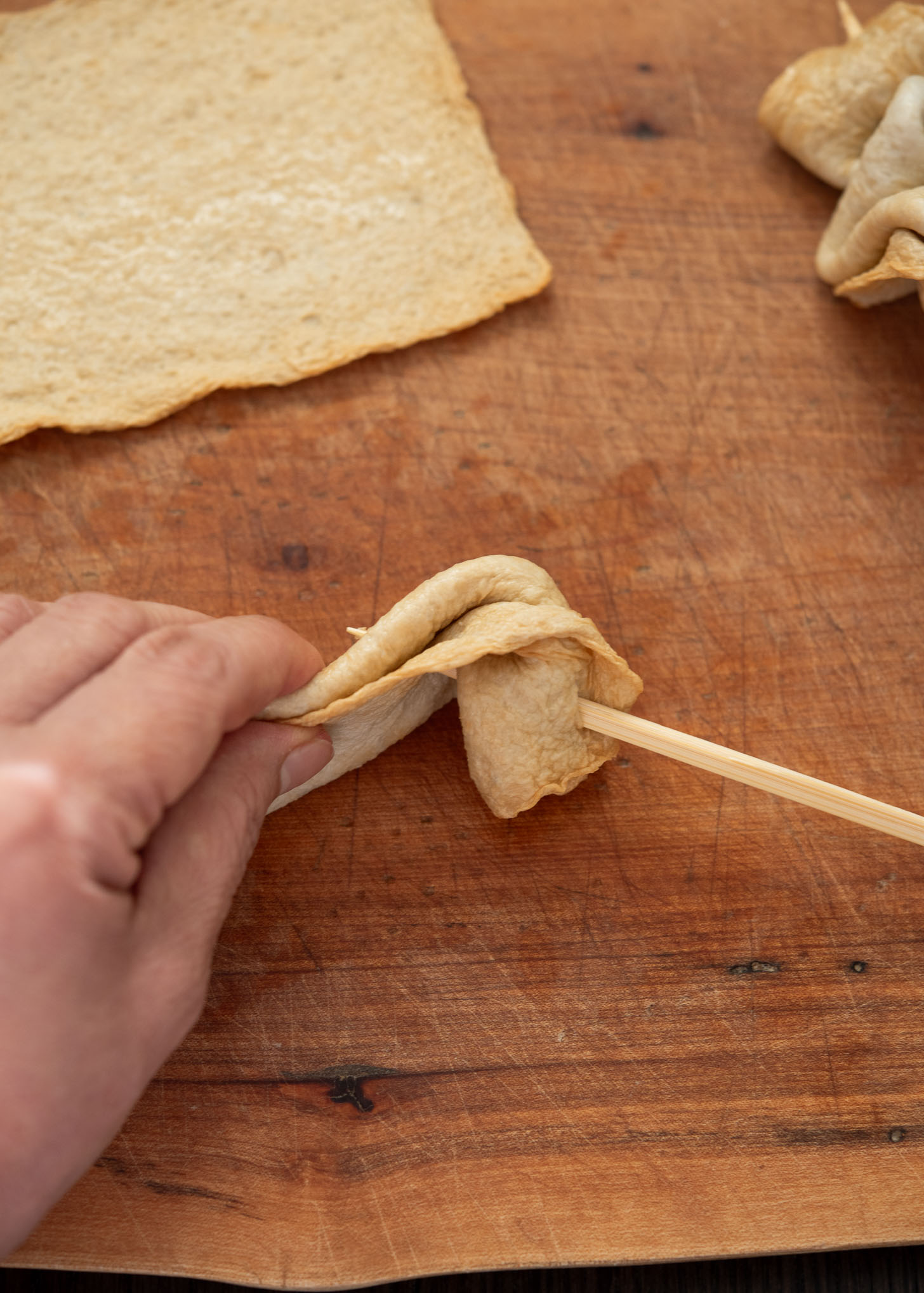 Inserting wooden a skewer to a folded fish cake sheet. 