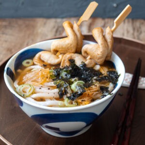 Kimchi udon noodle soup with fish cake skewers in a bowl.