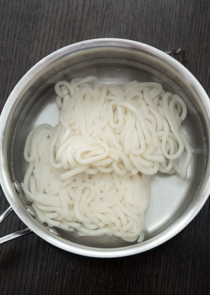 Frozen udon noodles added to boiling hot water.