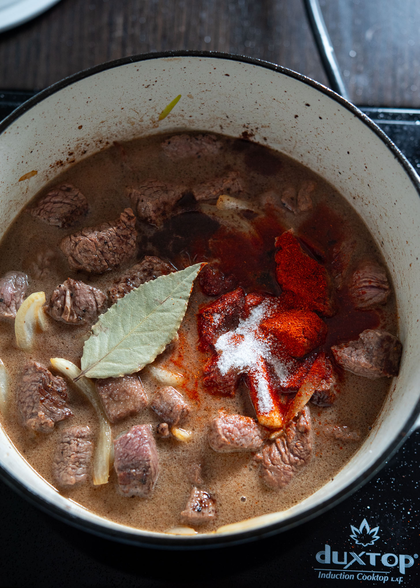 Adding browned beef with other stew ingredients in a pot.
