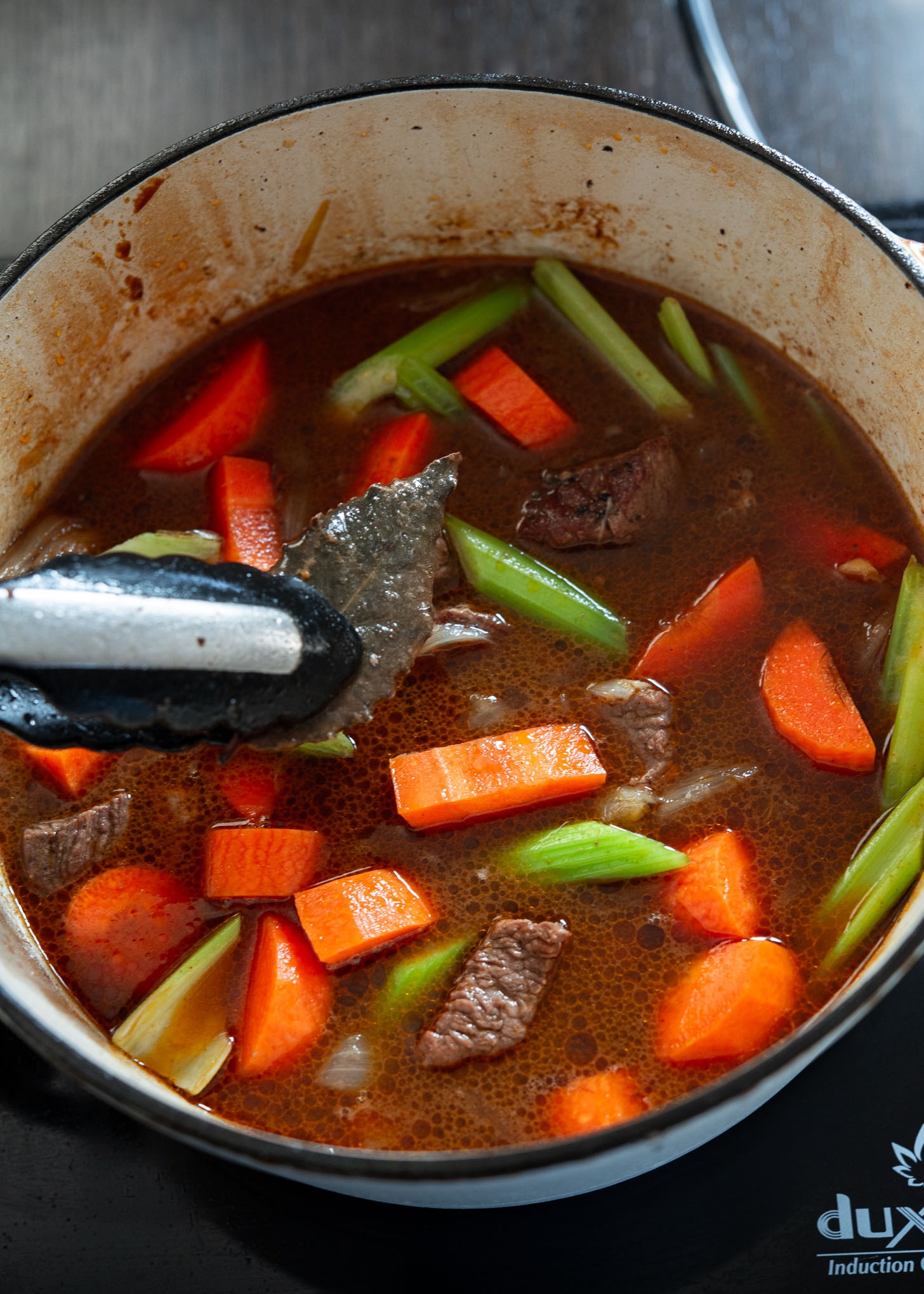 Removing a bay leaf and adding vegetables to the stew.