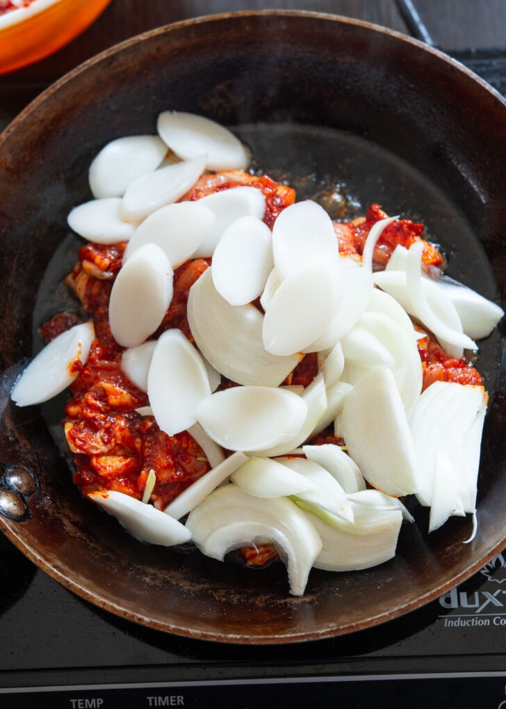 Rice cake rounds added to fire chicken marinade mixture in a skillet.