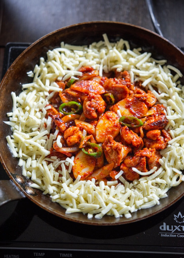 Shredded cheese placed around chicken in a skillet