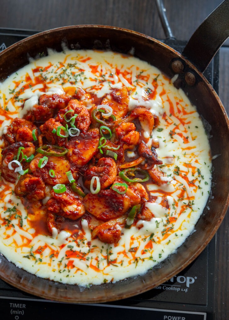Spicy fire chicken pieces over melted cheese in a skillet.