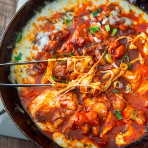 Korean fire chicken (buldak) with melted cheese in a skillet.