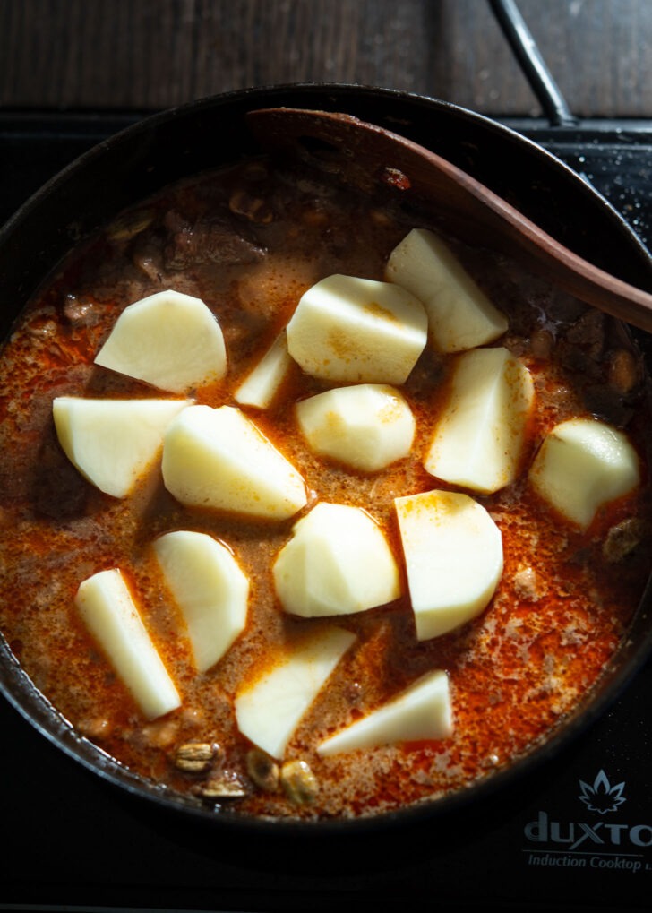 Potato chunks added to massaman curry sauce in a pot.