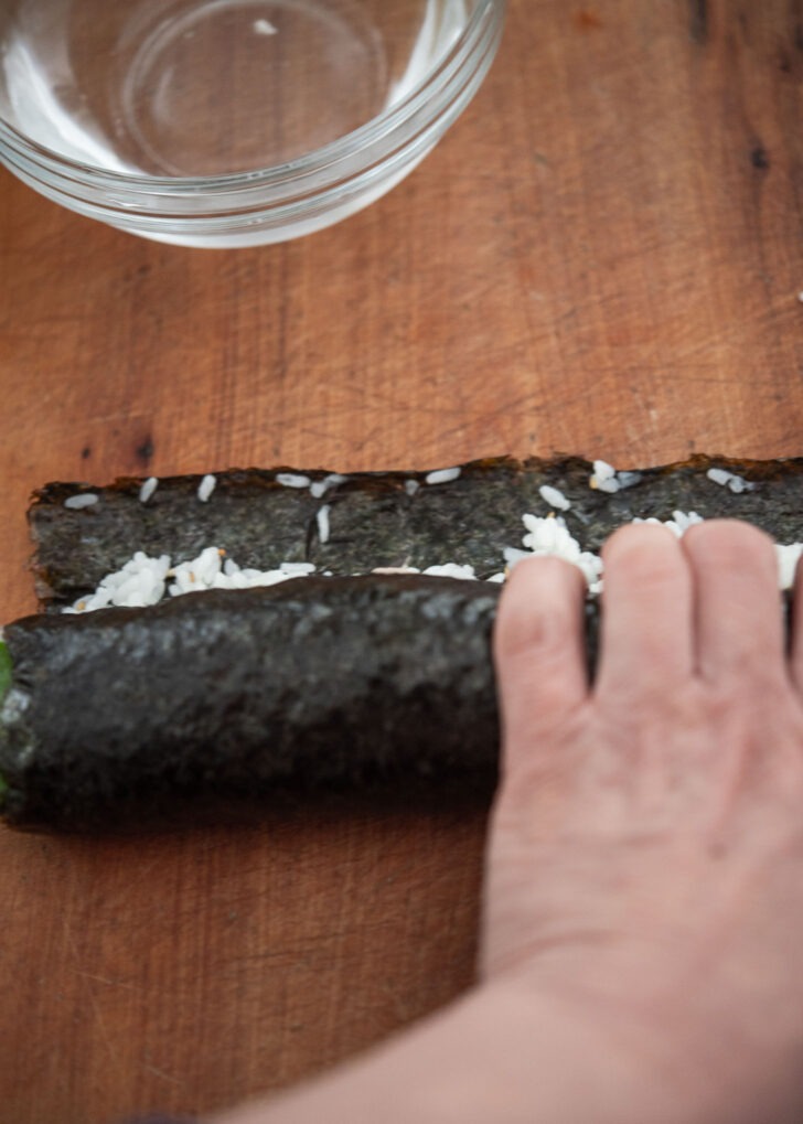 A hand rolling Korean seaweed rice roll in shape.
