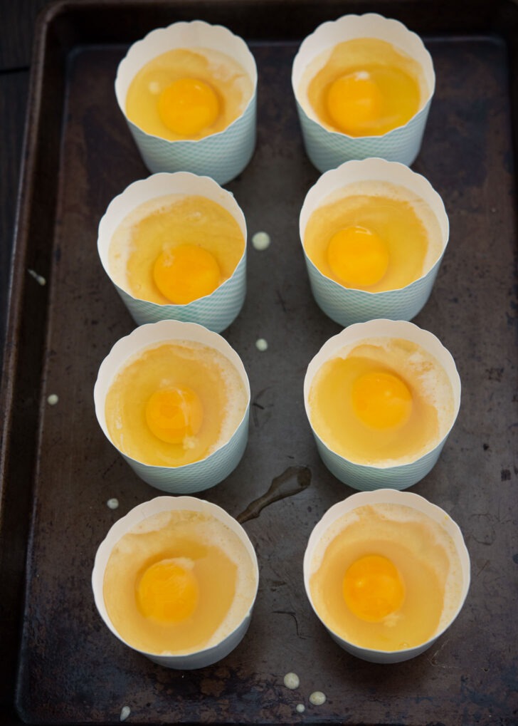 whole eggs topped on egg bread batter in baking cups.