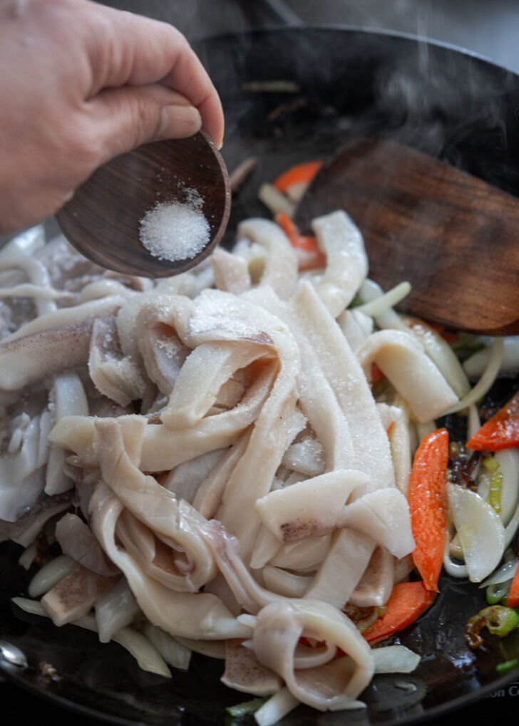 Squid pieces and sugar added to vegetables in a skillet.