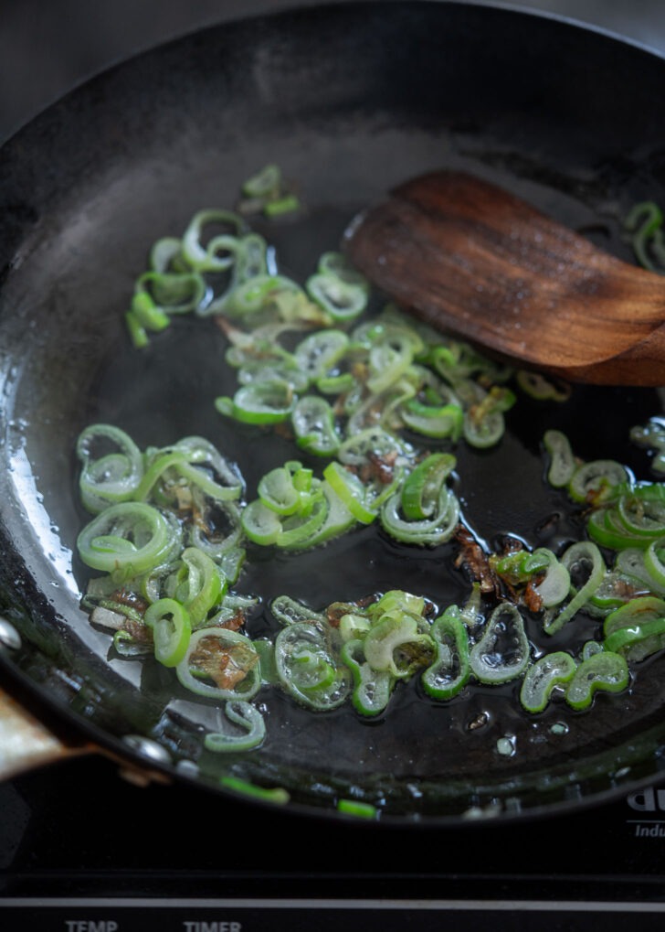 Asian leek is frying in oil until slightly charred.