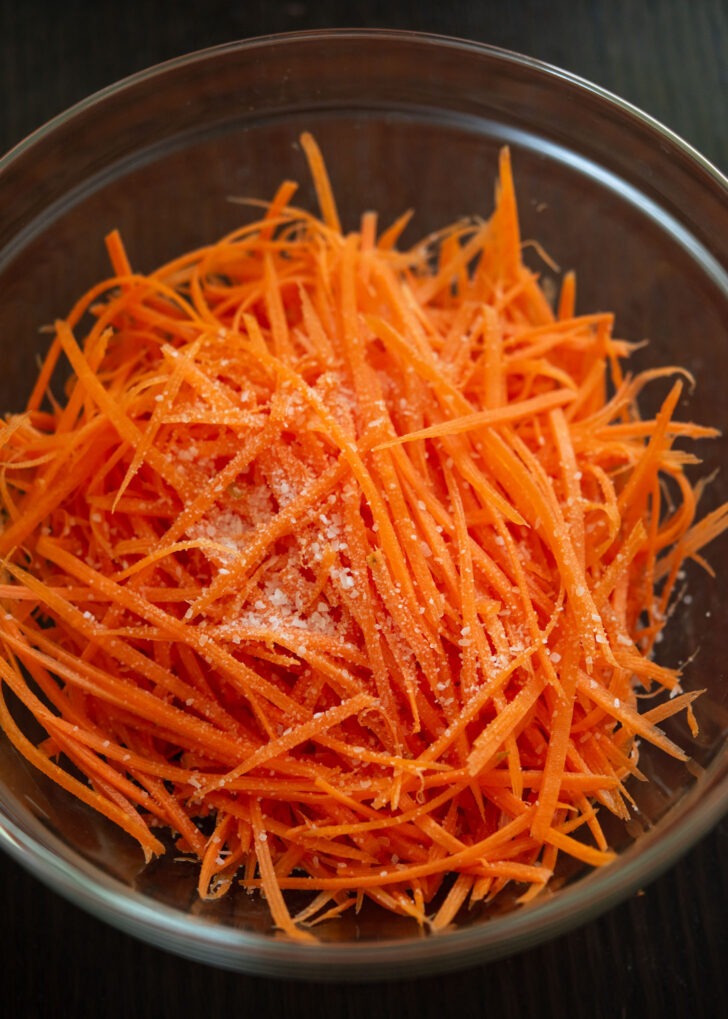 Julienned carrots with salt in a mixing bowl.