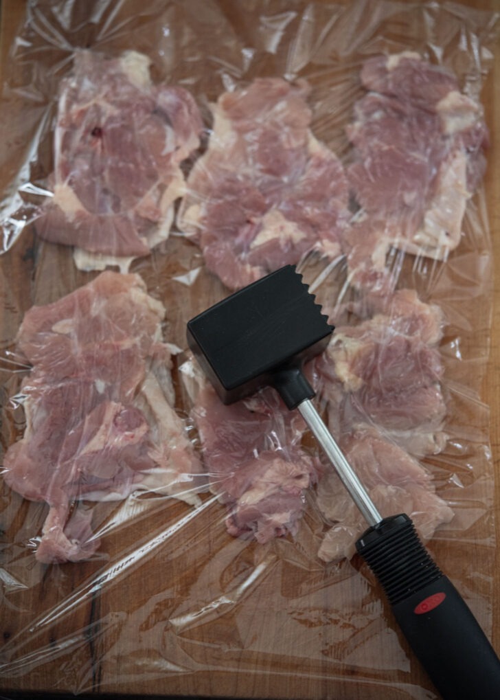 Pounding chicken thighs with a meat hammer.