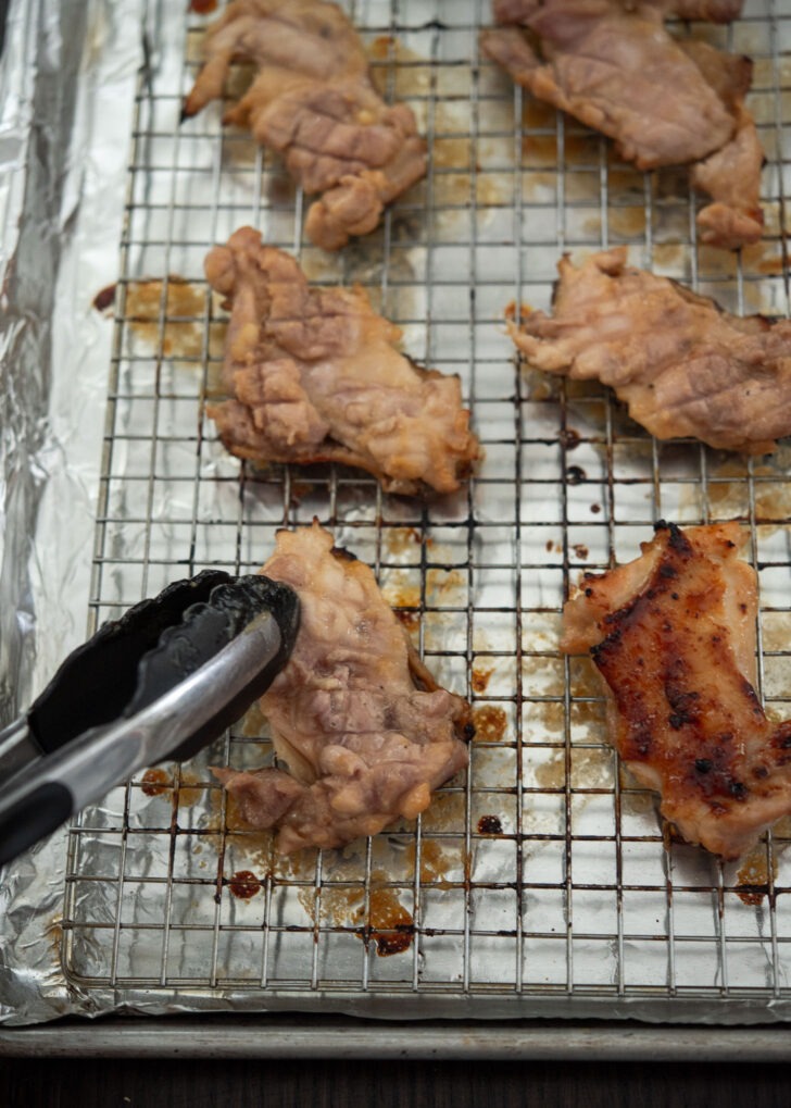 Flipping broiled chicken thighs to the other side.