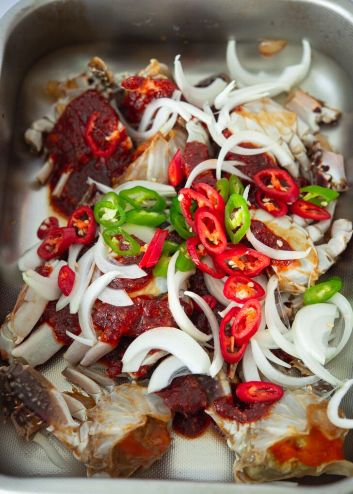 Sliced onion and fresh chili added to crab and spicy sauce in a container.