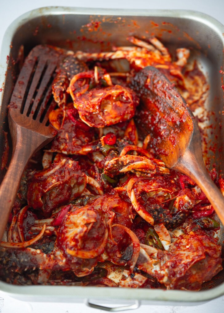 Two spatulas tossing crab with spicy sauce.