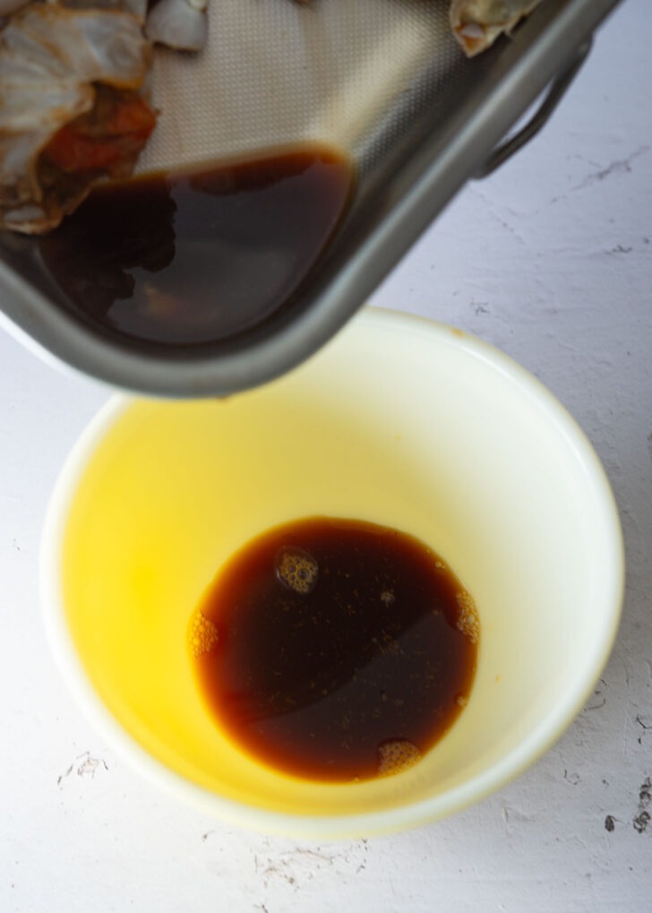 Collecting soy sauce marinade from crab in a bowl.