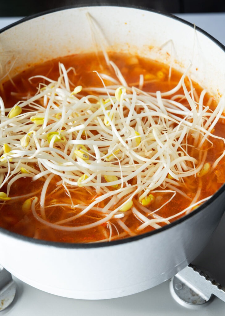 Soybean sprouts added to kimchi soup in a pot.