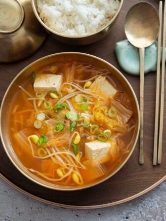 A bowl of kimchi soybean sprout soup served on a tray.