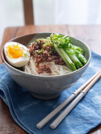 A bowl of noodles with ground beef sauce, cucumber, and hard boiled egg.