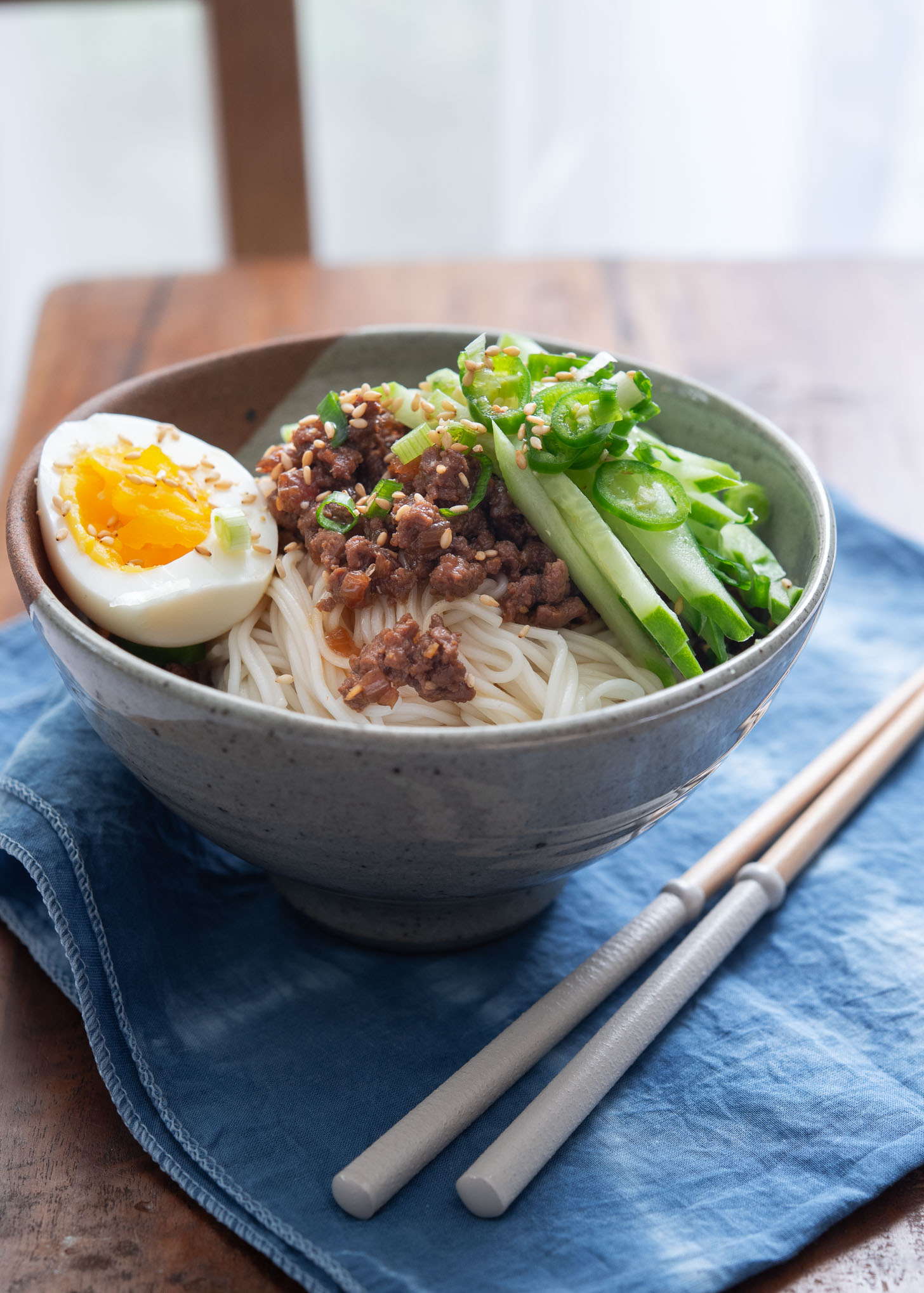 A bowl of ground beef noodles topped with cucumber, and hard boiled egg.