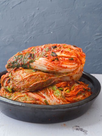 Several whole cabbage kimchi stacked up in a container.