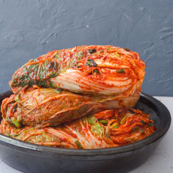 Several whole cabbage kimchi stacked up in a container.