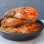 Whole cabbage kimchi stacked up in a container.