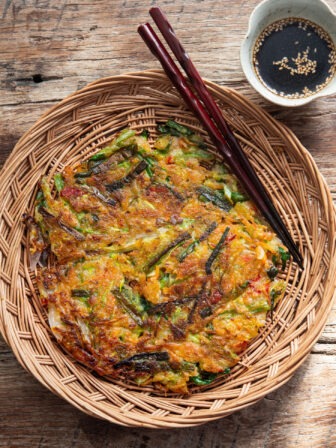Crispy Korean vegetable pancake (yachaejeon) on a woven basket plate.