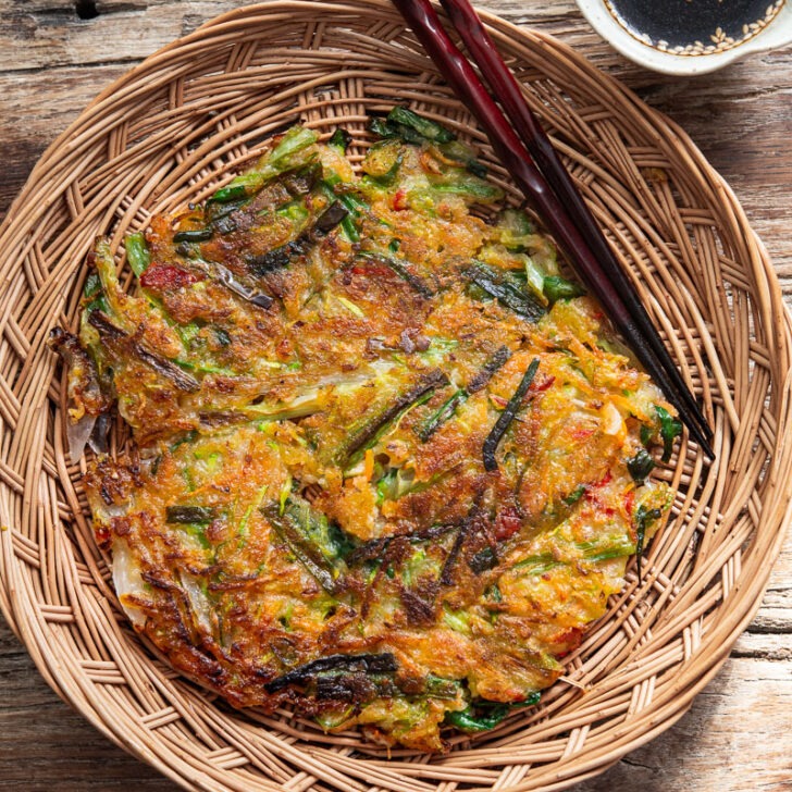 Crispy Korean vegetable pancake (yachaejeon) on a woven basket plate.