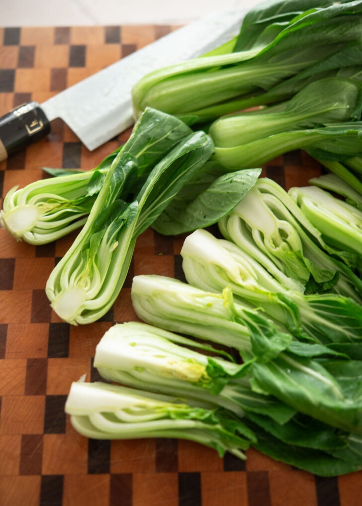 Fresh bok choy cut in half lengthwise showing crisp white stems and green leaves.