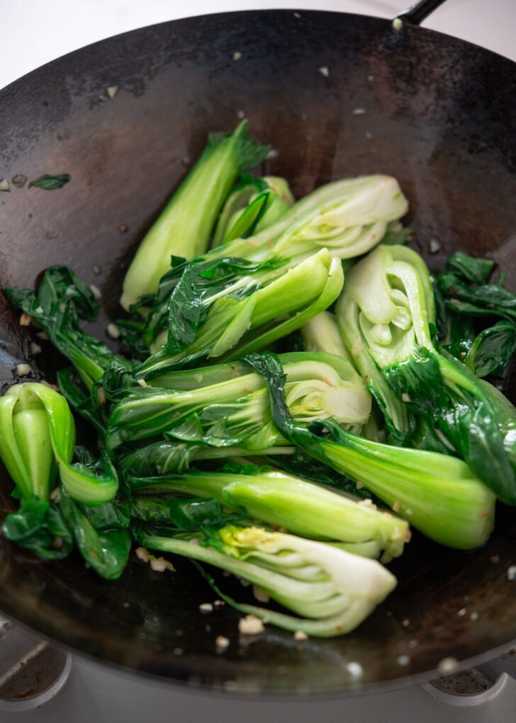 Bok choy stir-fried with garlic in hot oil in a wok, just starting to wilt.